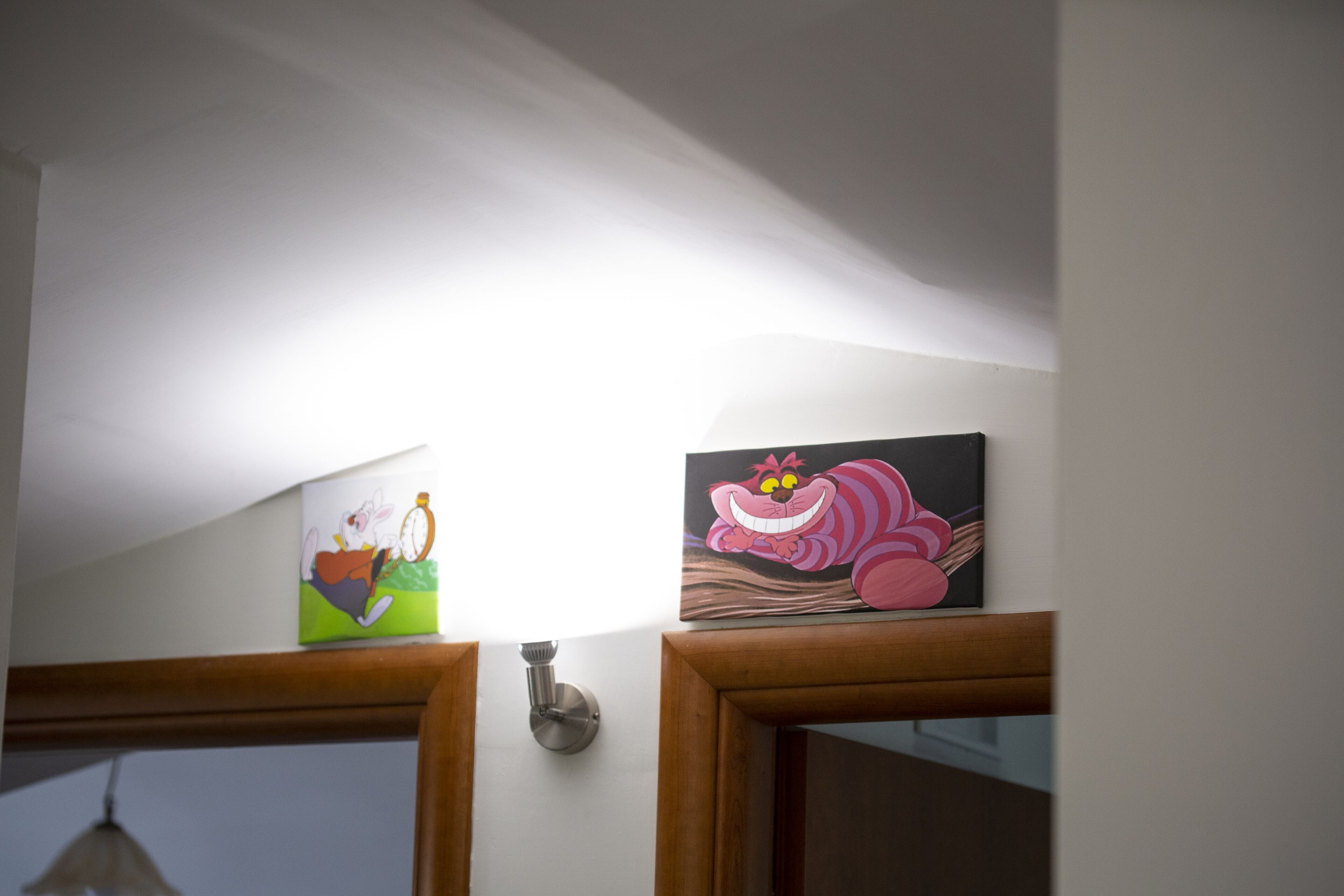 Una habitación con un marco de puerta de madera, una lámpara y dos obras de arte colgadas en la pared.