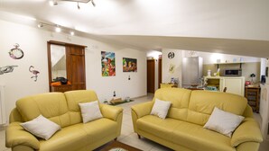 A living room with two yellow sofas, a wooden cabinet, and a kitchen area with a microwave and refrigerator. - B&B Delle Meraviglie (Pellezzano)