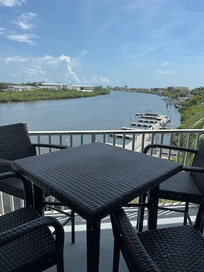 A balcony with wicker furniture overlooking a river, docks, and buildings in the distance.