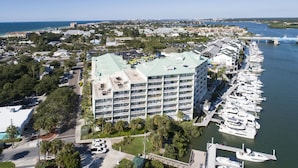 A multi-story hotel with balconies overlooking a marina, adjacent to a coastal road and a marina with numerous boats. - Waterfront Condo+4 FREE Waterpark Passes-Walk to Beach-Family Favorite-Sleeps 8 (Indian Rocks Beach)