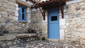 Un edificio de piedra con puerta y ventana azules, un patio empedrado y una pérgola de madera.