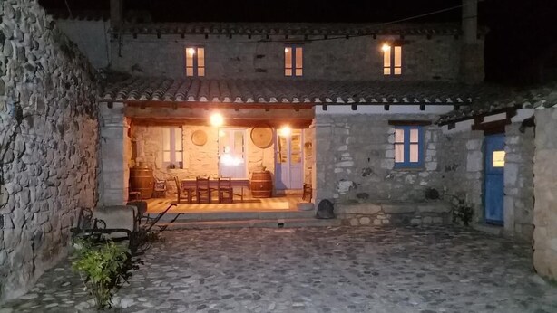 Un edificio de piedra con un patio, una zona de comedor con mesas y sillas, y una puerta azul.