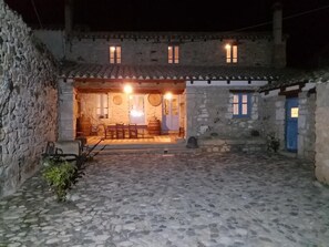 Un edificio de piedra con un patio, una zona de comedor con mesas y sillas, y una puerta azul.