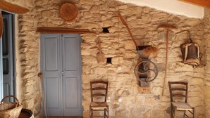 Una habitación rústica con pared de piedra, techo de madera, una puerta azul y dos sillas de madera.
