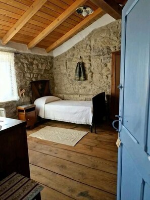 Quarto com teto de madeira, paredes de pedra, cama, mesa de cabeceira e guarda-roupa.