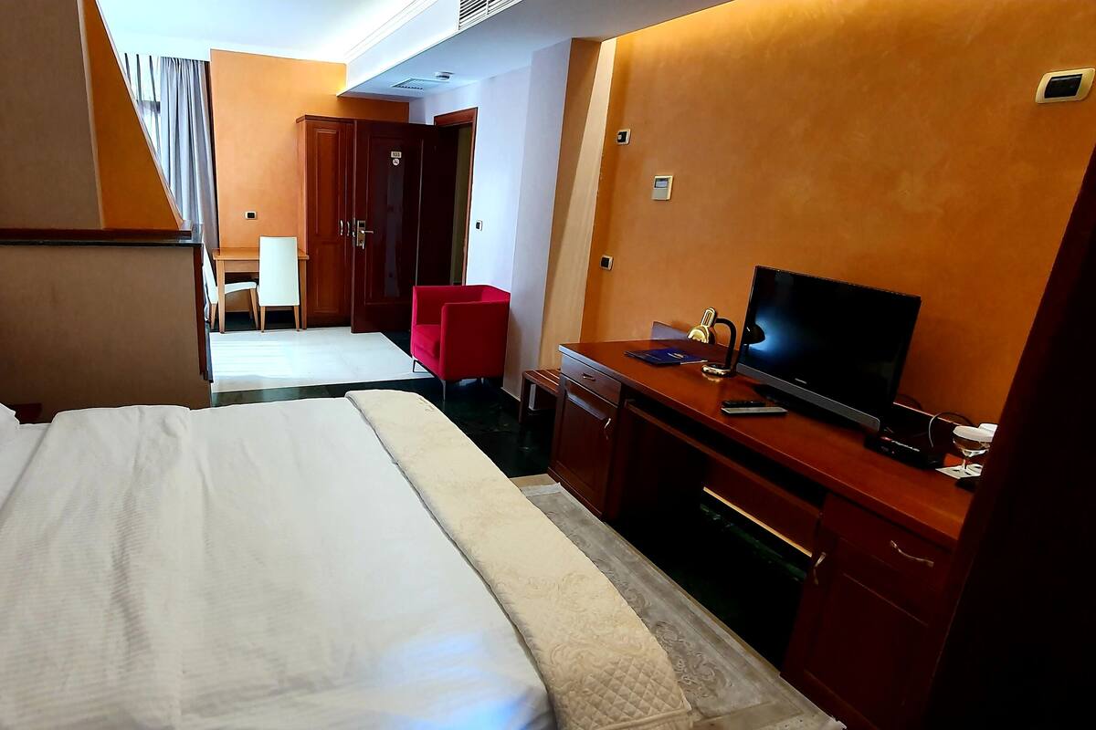 A hotel room with a large bed, a desk with a TV, and a red chair.