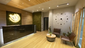 A modern reception area with a wooden floor, a reception desk, a wall clock, and a seating area with chairs and a round table. - Nov Hotel (Tirana)