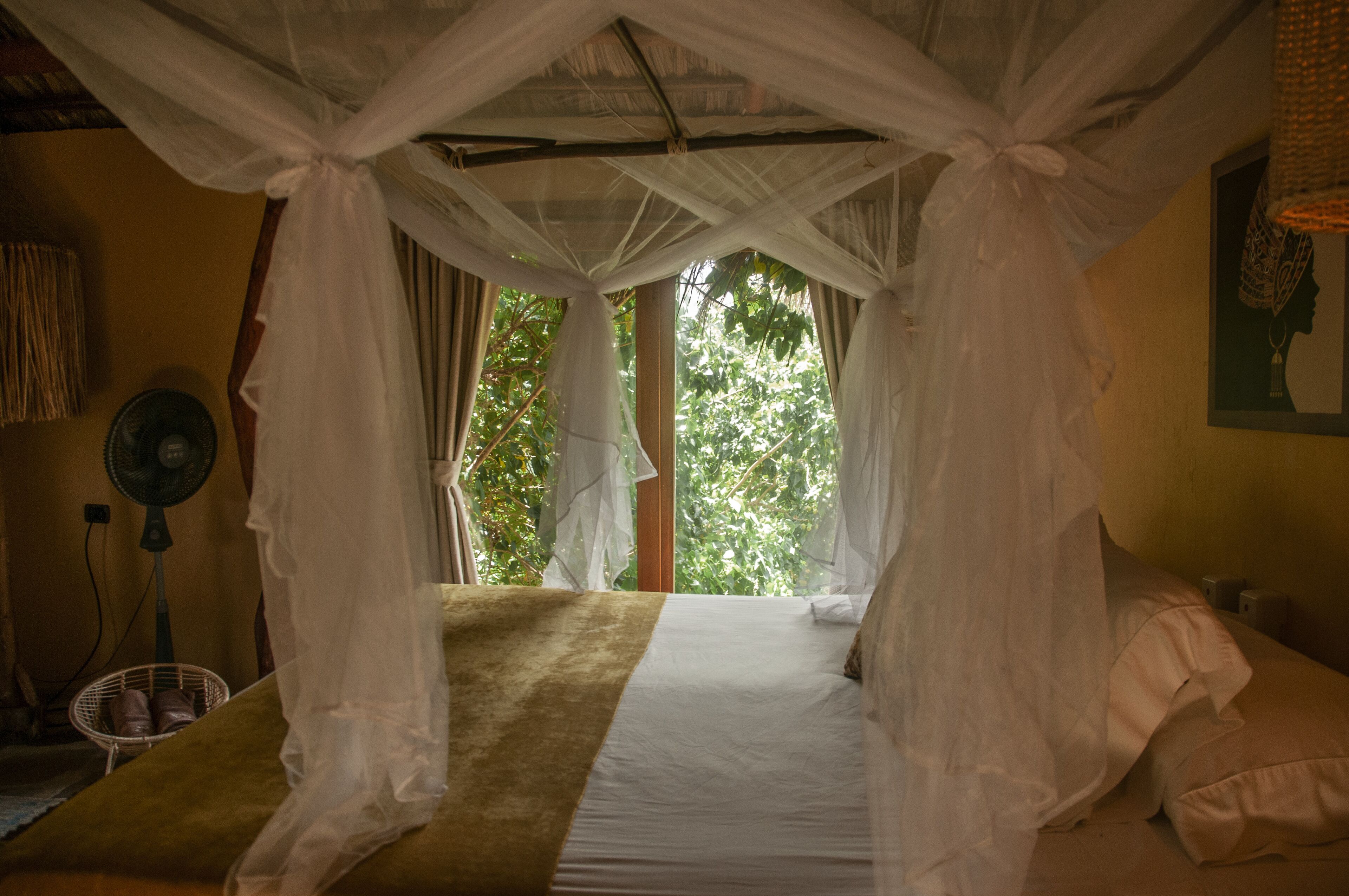 Una habitación con cama bajo un dosel, un ventilador y una ventana con cortinas.