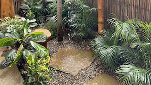 A bamboo shower enclosure with a water feature, surrounded by tropical plants and a bamboo fence.