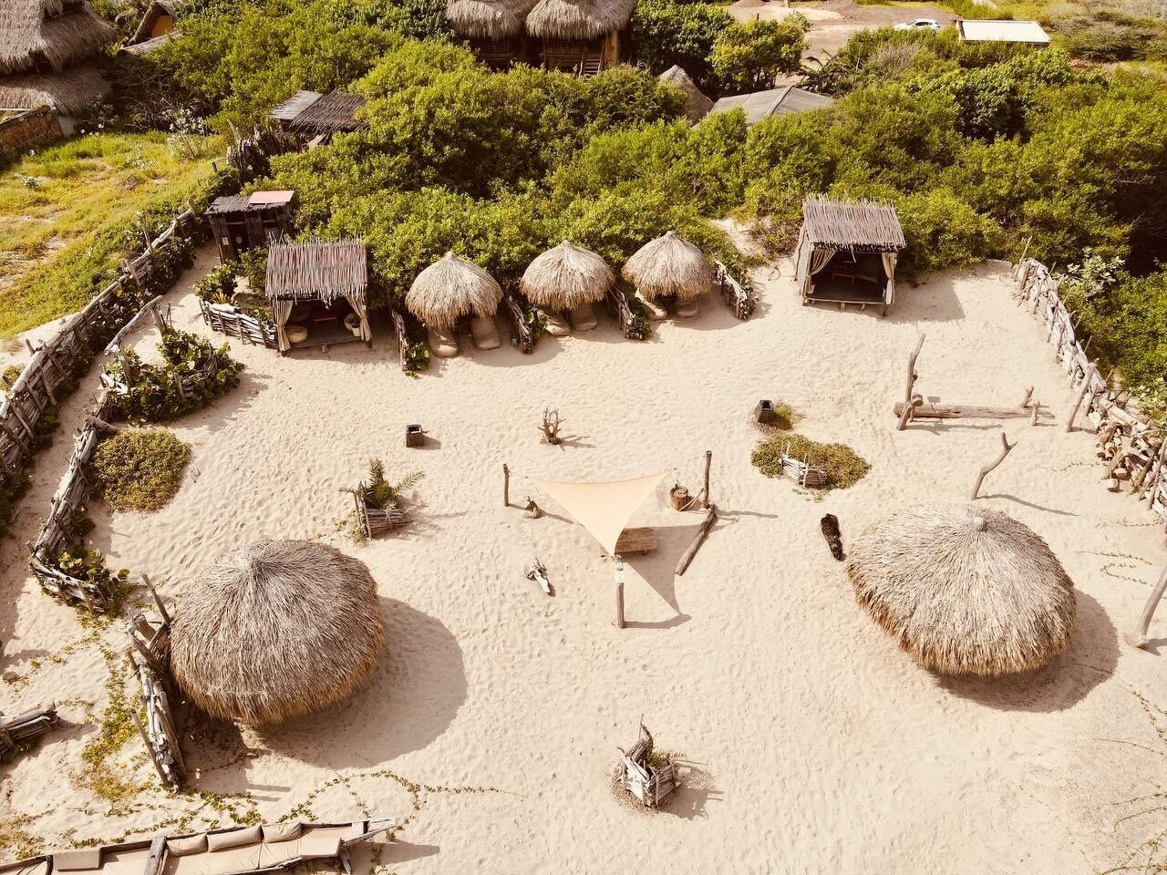 A sandy area with thatched-roof huts and a wooden fence.