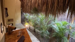 A room with a thatched roof, a wooden bench, and potted plants.