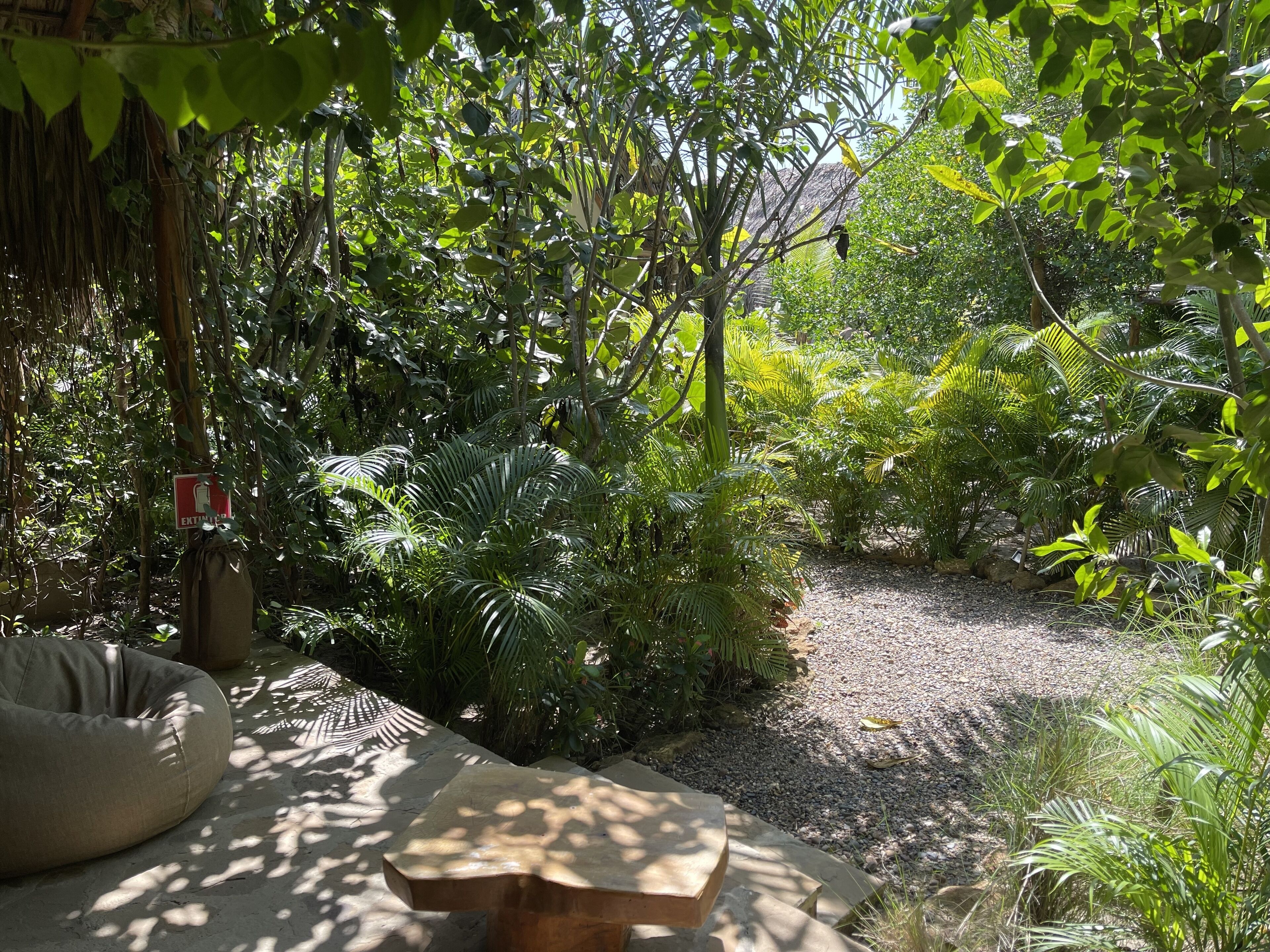 Un jardín con un banco de hormigón, una mesita y un cartel que indica un baño.