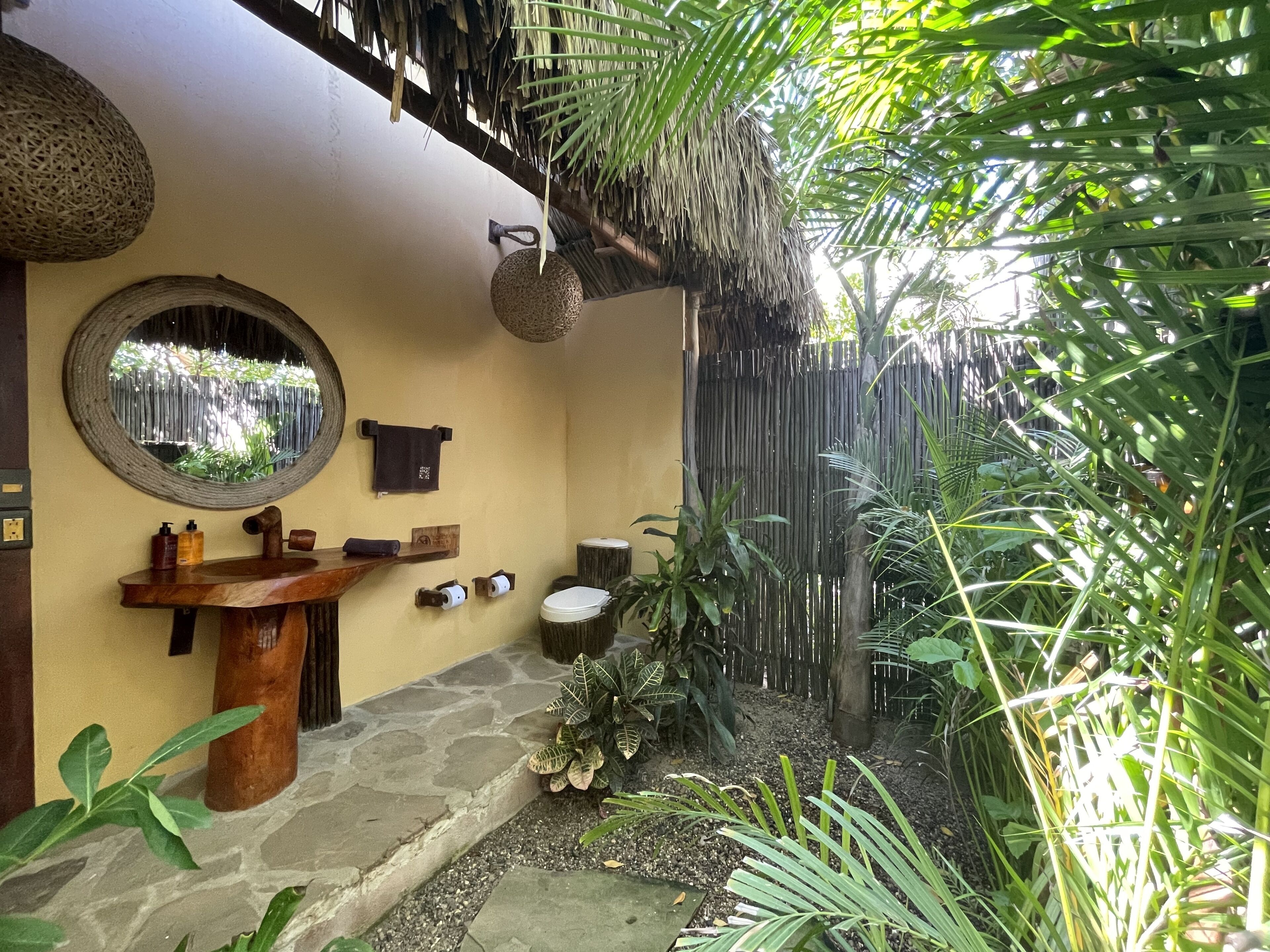 A bathroom with a stone sink, a mirror, and a wooden shelf with toiletries.
