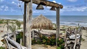 A beach hut with a thatched roof, surrounded by wooden logs and plants, overlooking the ocean.