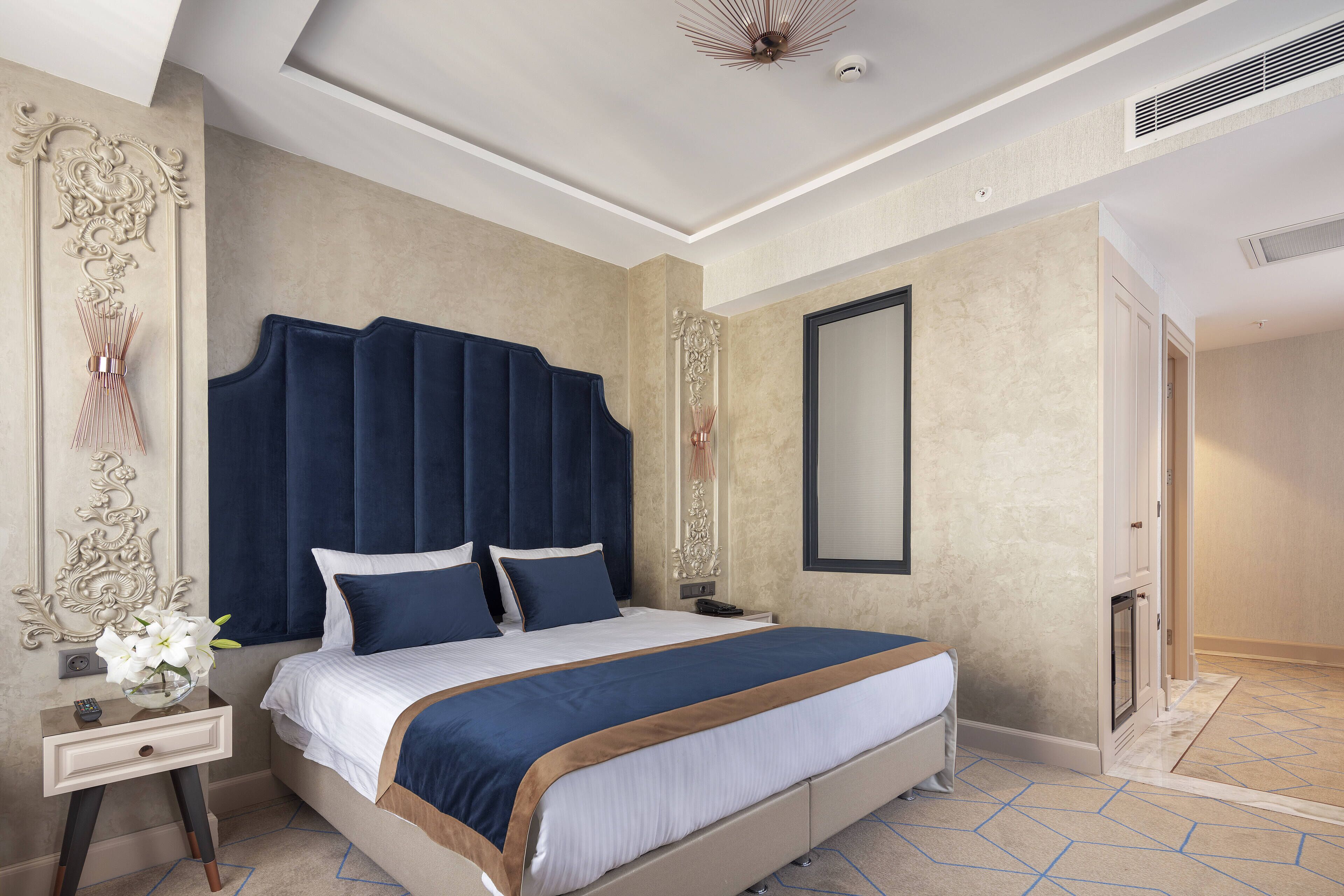 A modern hotel room with a large bed, a nightstand, a mirror, and a decorative wall panel.