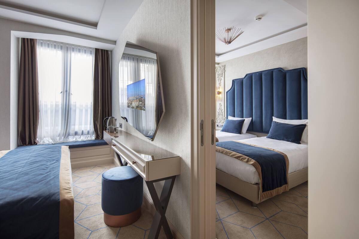 Habitación de hotel con cama, escritorio, silla, ventana con cortinas y cabecera.