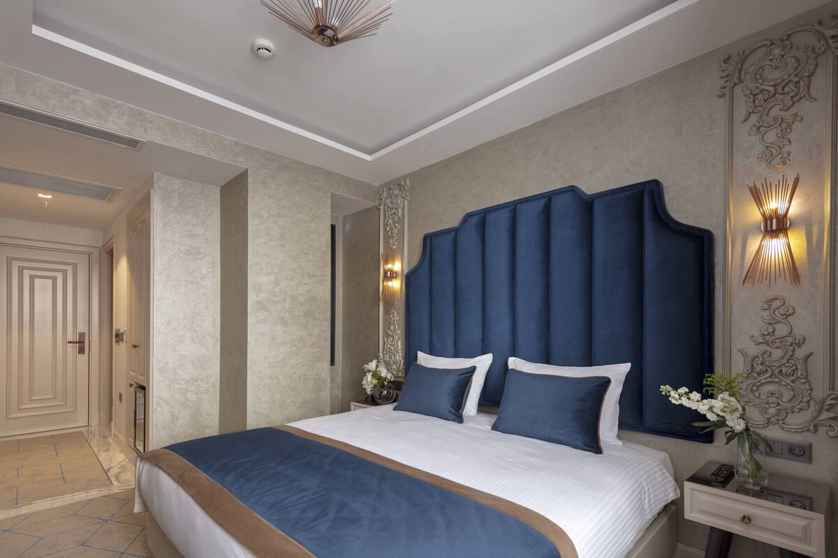 Una habitación de hotel moderna con una cama grande, una mesita de noche con lámpara y un panel decorativo en la pared.