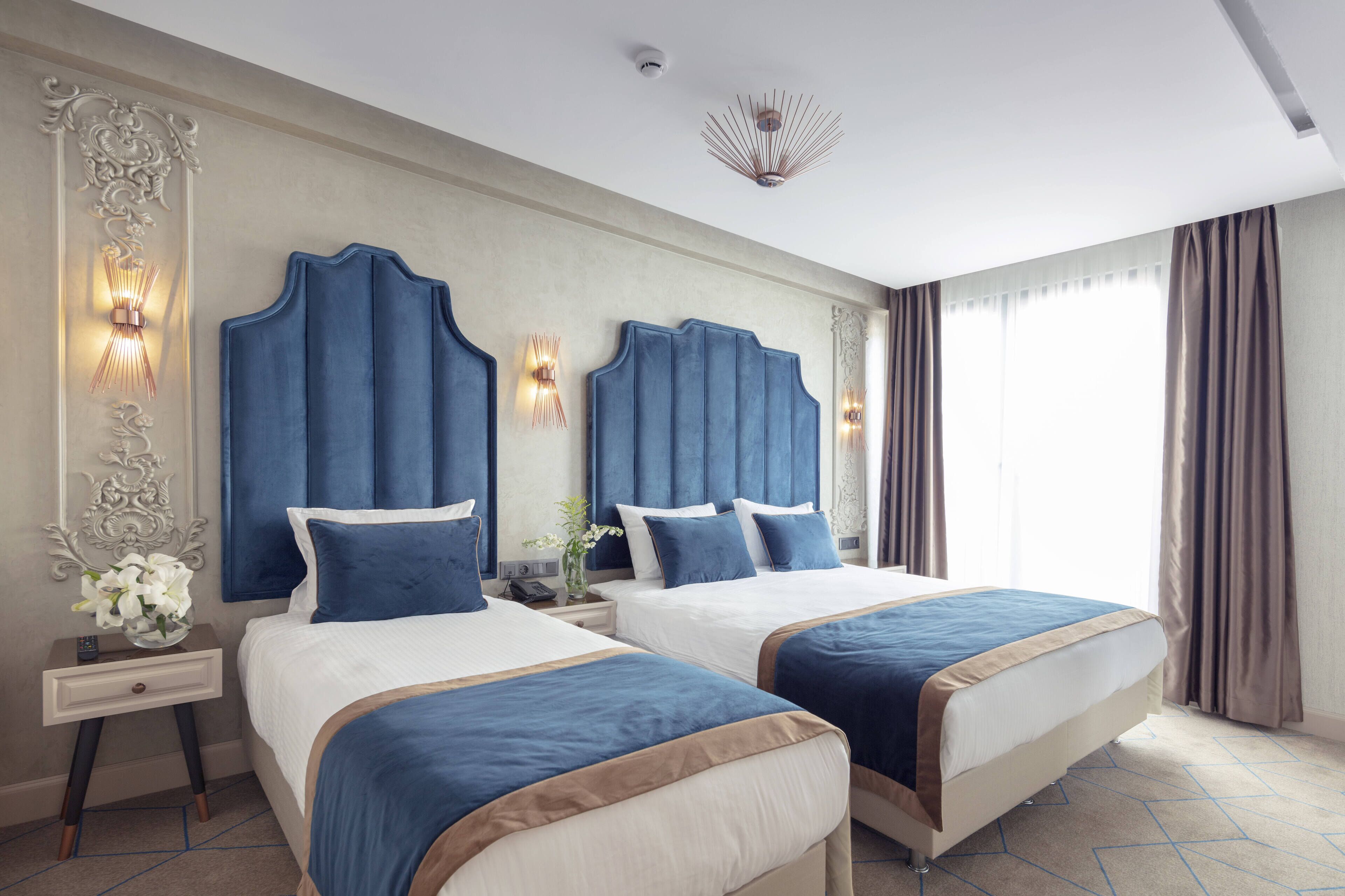 A hotel room with two beds, a nightstand with a vase of flowers, and a decorative wall panel.