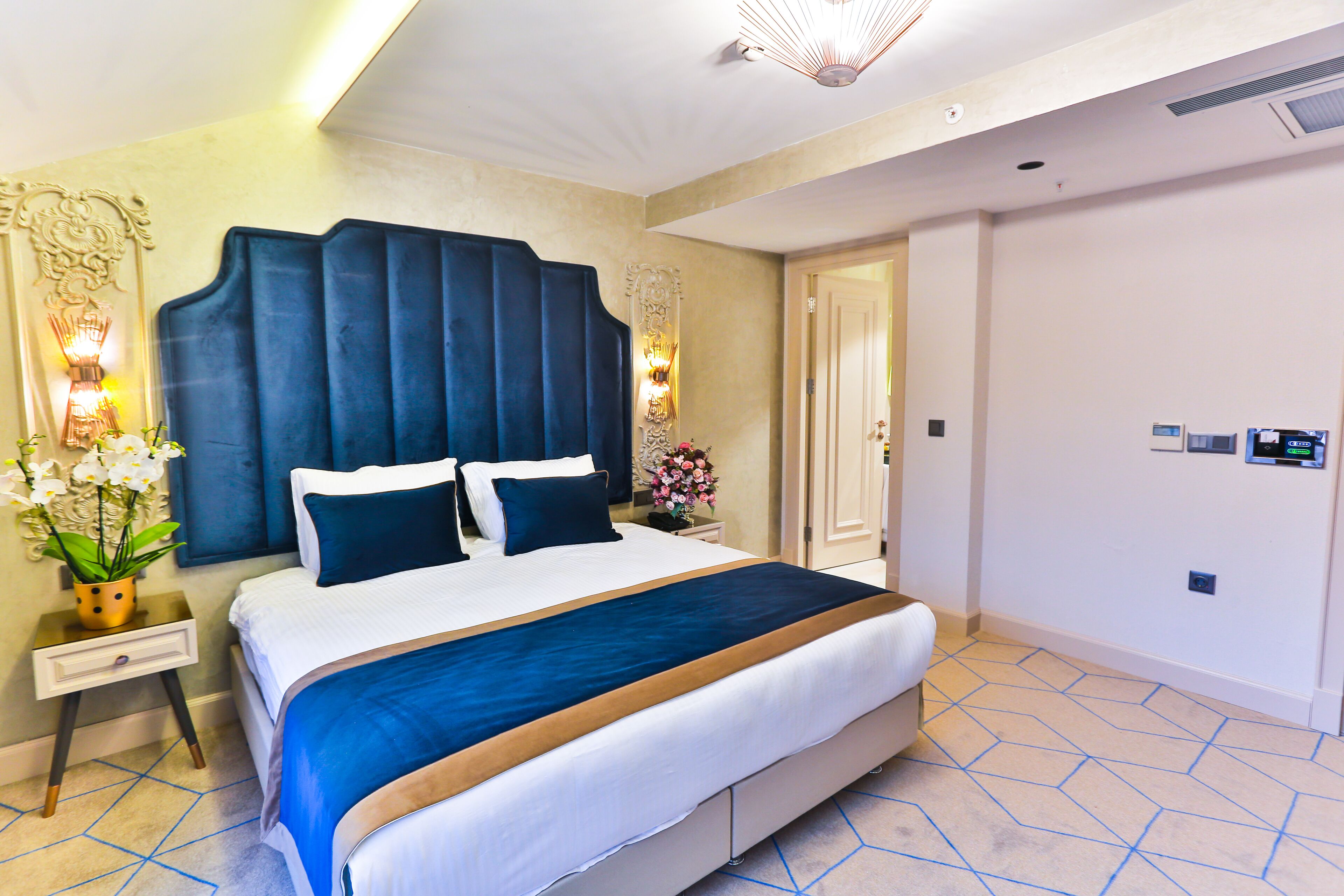 Une chambre d’hôtel avec un grand lit, une table de chevet, une lampe fixée au mur et une porte.