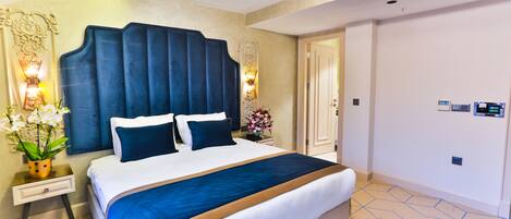 A hotel room with a large bed, a nightstand, a wall-mounted lamp, and a door.