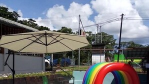 Een zwembad met een opblaasbare glijbaan in de vorm van een regenboog, een schaduwrijk gedeelte en uitzicht op de omgeving.
