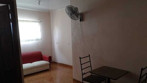 Een kamer met een rode bank, een eettafel met stoelen en een ventilator aan de muur.