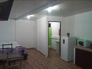 A small, compact room with a bed, a desk, and a kitchenette. - Palacios Arenal - Hostel (La Fortuna)