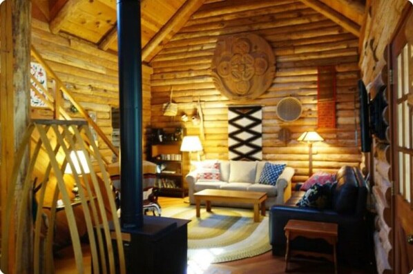 Cozy cabin interior with a central seating area, bookshelf, and wooden staircase.
