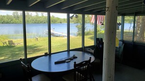A room with large windows overlooking a lake, a round table with chairs, and a flag outside. - Cabin on lake close to ATV & snowmobile trails (Bigfork)