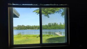 A window with a view of a lake, grassy area, and a dock. - Cabin on lake close to ATV & snowmobile trails (Bigfork)