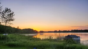 A serene lakeside setting with a campfire, two chairs, and a boat docked near the water. - Cabin on lake close to ATV & snowmobile trails (Bigfork)