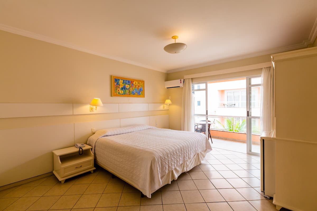 Habitación de hotel con cama, lámparas de noche, una mesita, un cuadro y vistas al exterior.