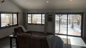 A cozy living room with a brown leather sofa, a coffee table, and a large window with a view of a snowy landscape.