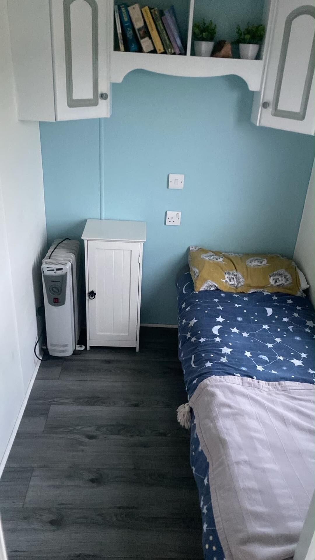 Een slaapkamer met een bed, een kachel, een kast en een plank met boeken en planten.
