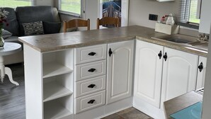 Una cocina compacta con armarios blancos, una isla integrada con cajones, una ventana con persianas y vistas al exterior.