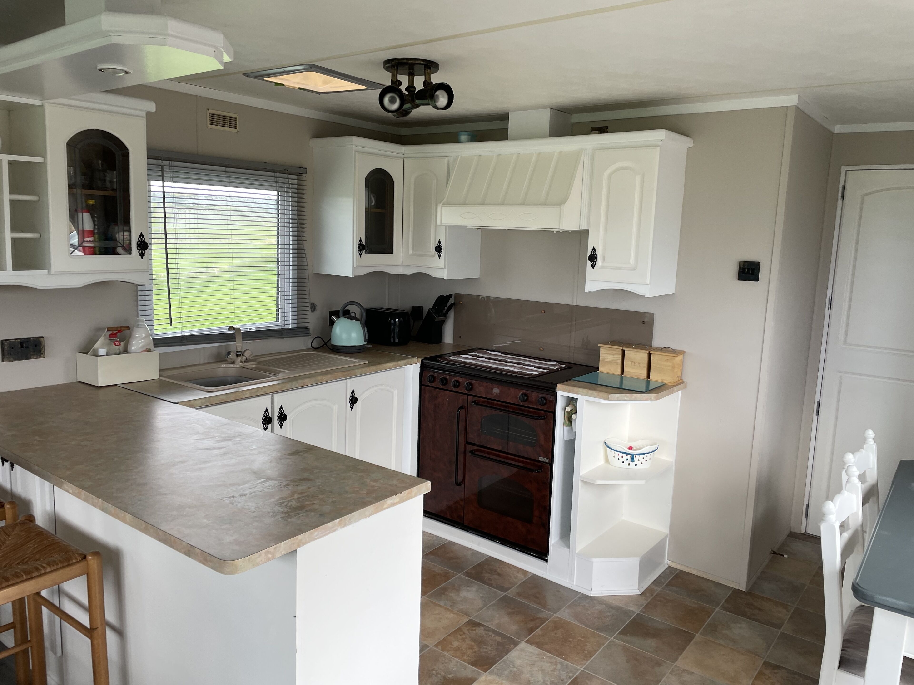A compact kitchen with white cabinetry, a built-in oven, a stove, and a window with blinds.