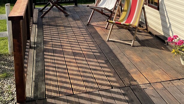 Una terraza con piso de madera, una mesa y dos sillas de playa.