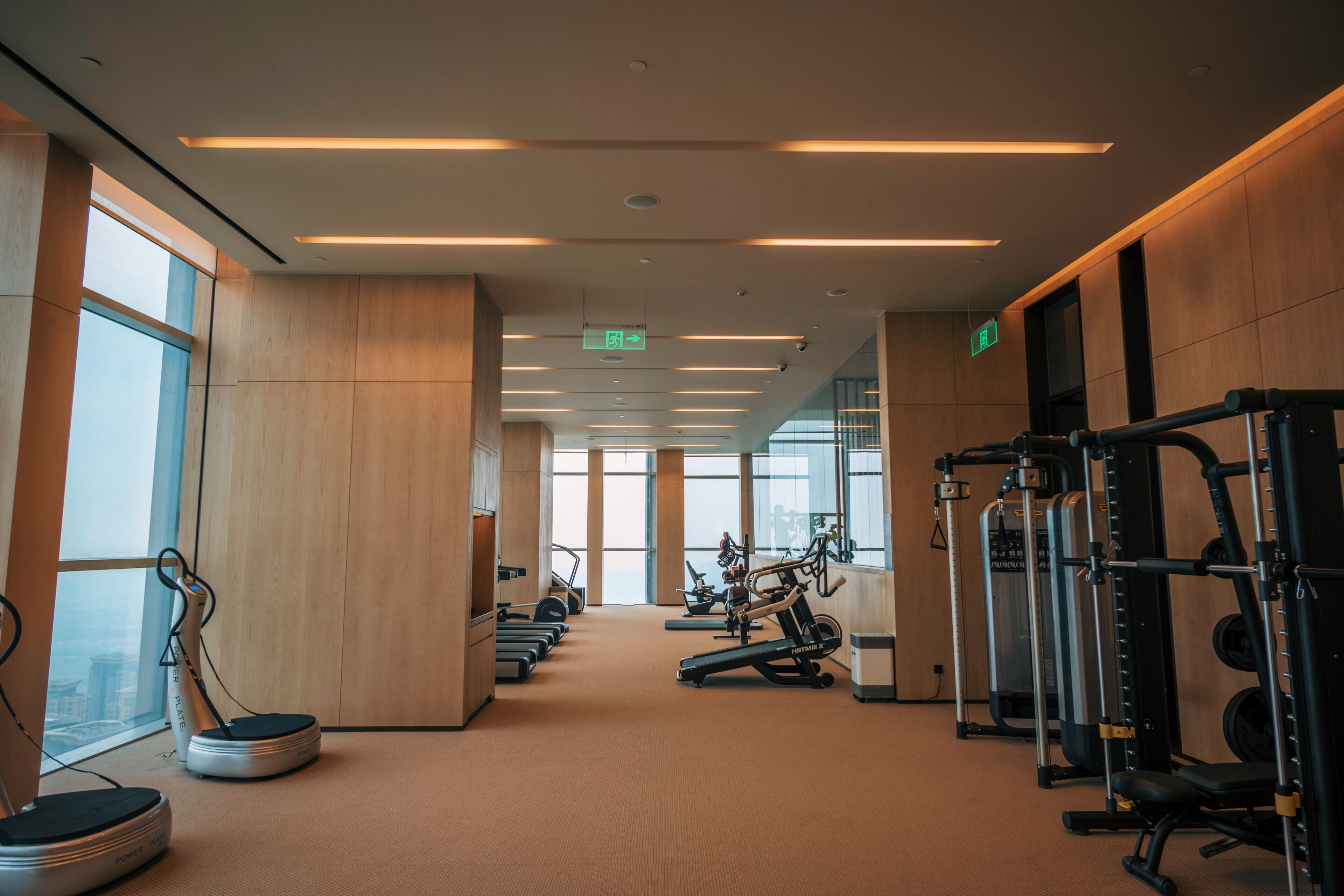 Un gimnasio con equipo de ejercicio, ventanas amplias y suelo alfombrado.
