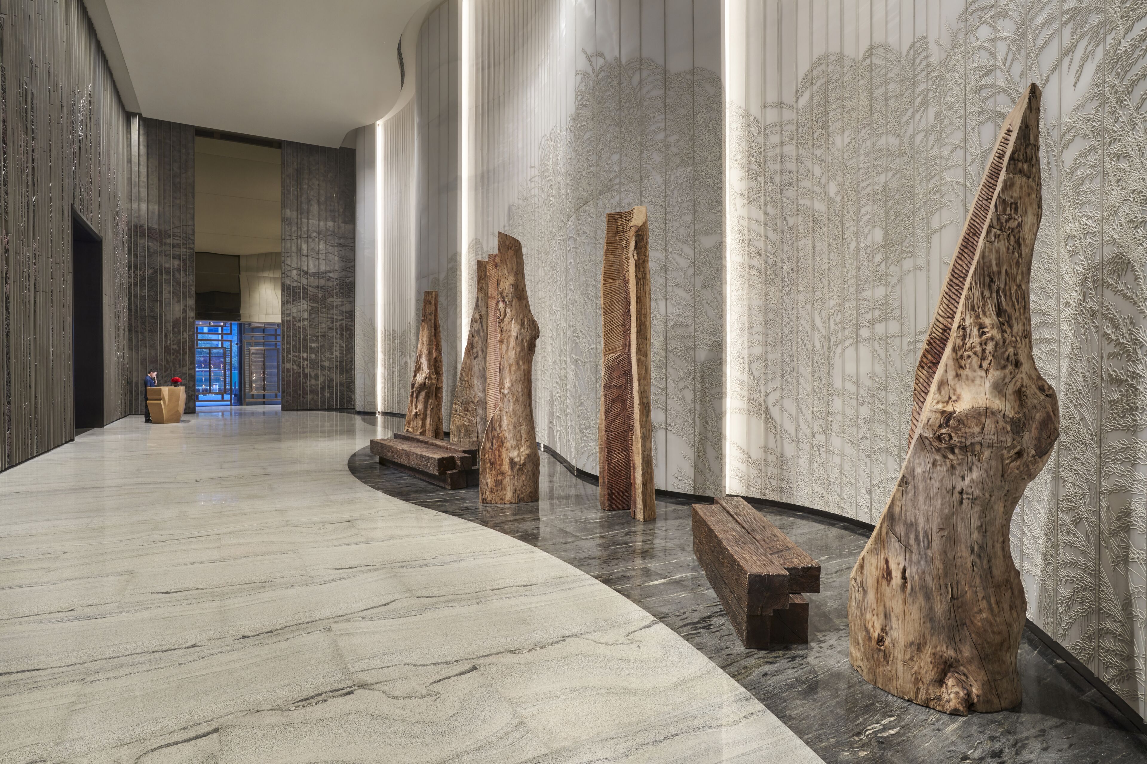 Un moderno vestíbulo con suelo de mármol, esculturas de madera y papel tapiz de diseño vertical.