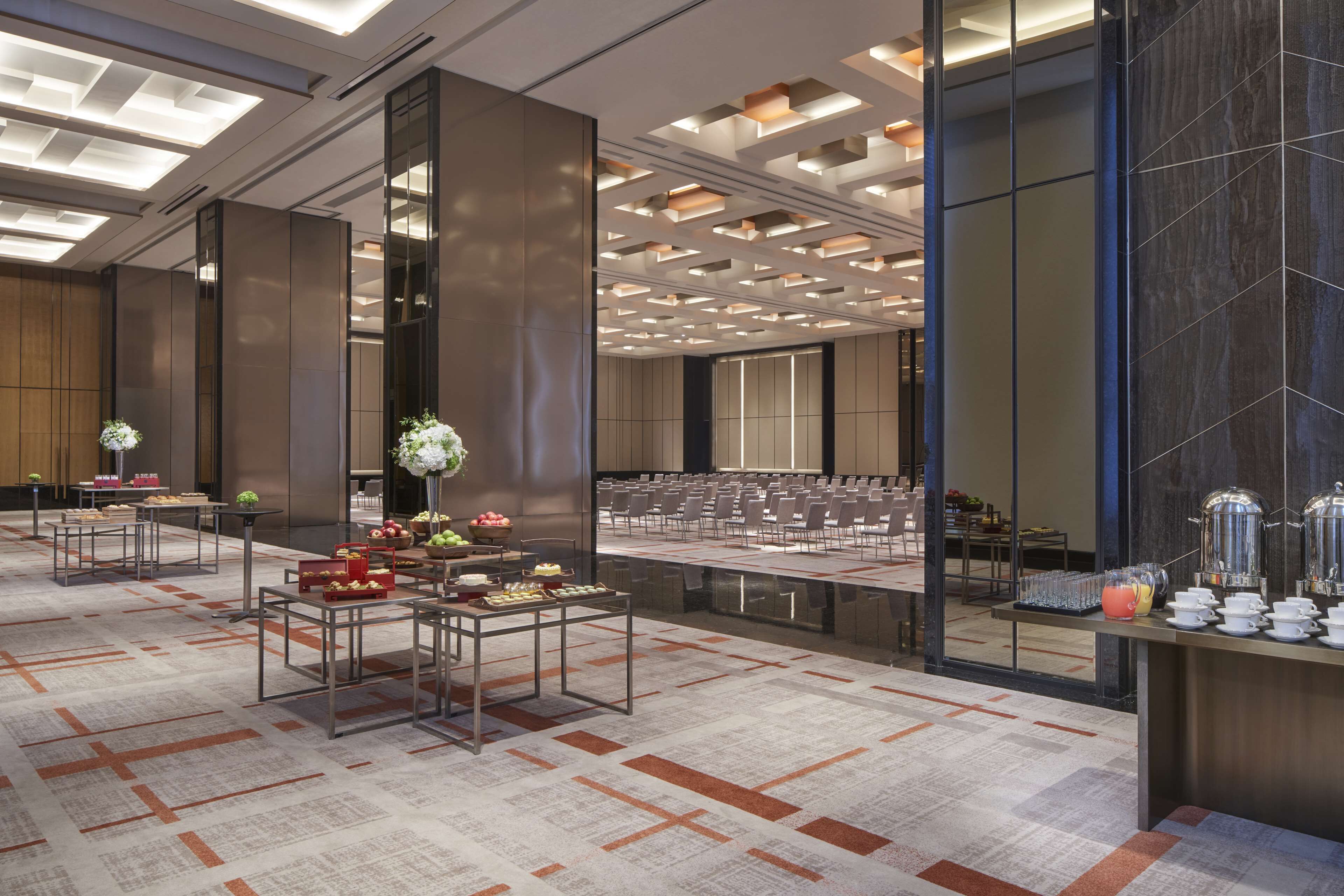 A modern hotel lobby with a buffet area, seating arrangements, and a large conference room.