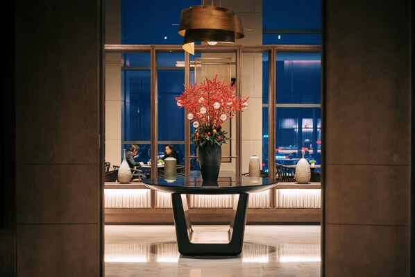 A modern interior with a round table, a vase with red flowers, and a hanging light fixture. - Grand Hyatt Hefei (Hefei)