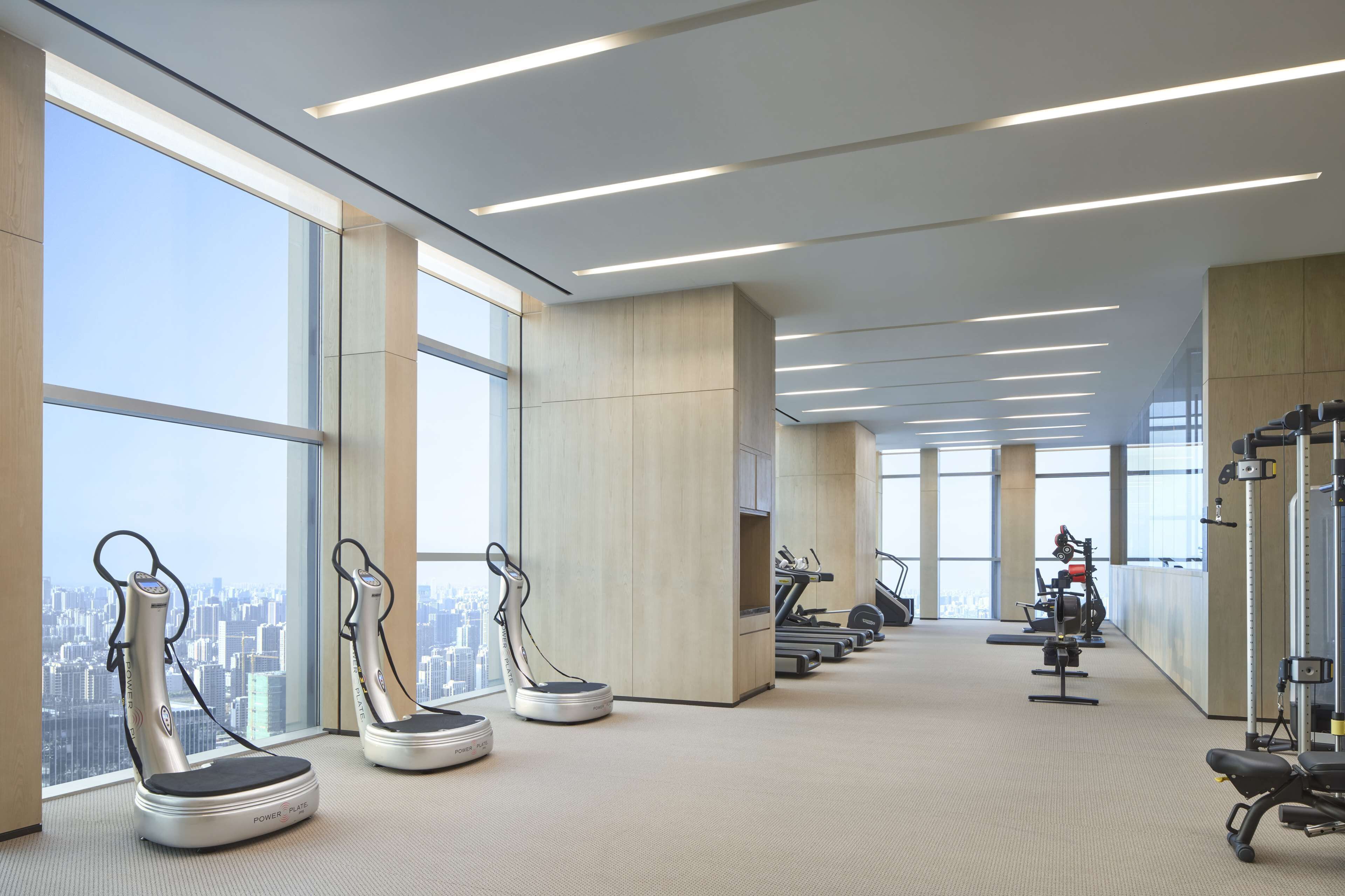 Ett modernt gym med träningsutrustning, stora fönster och utsikt över staden.