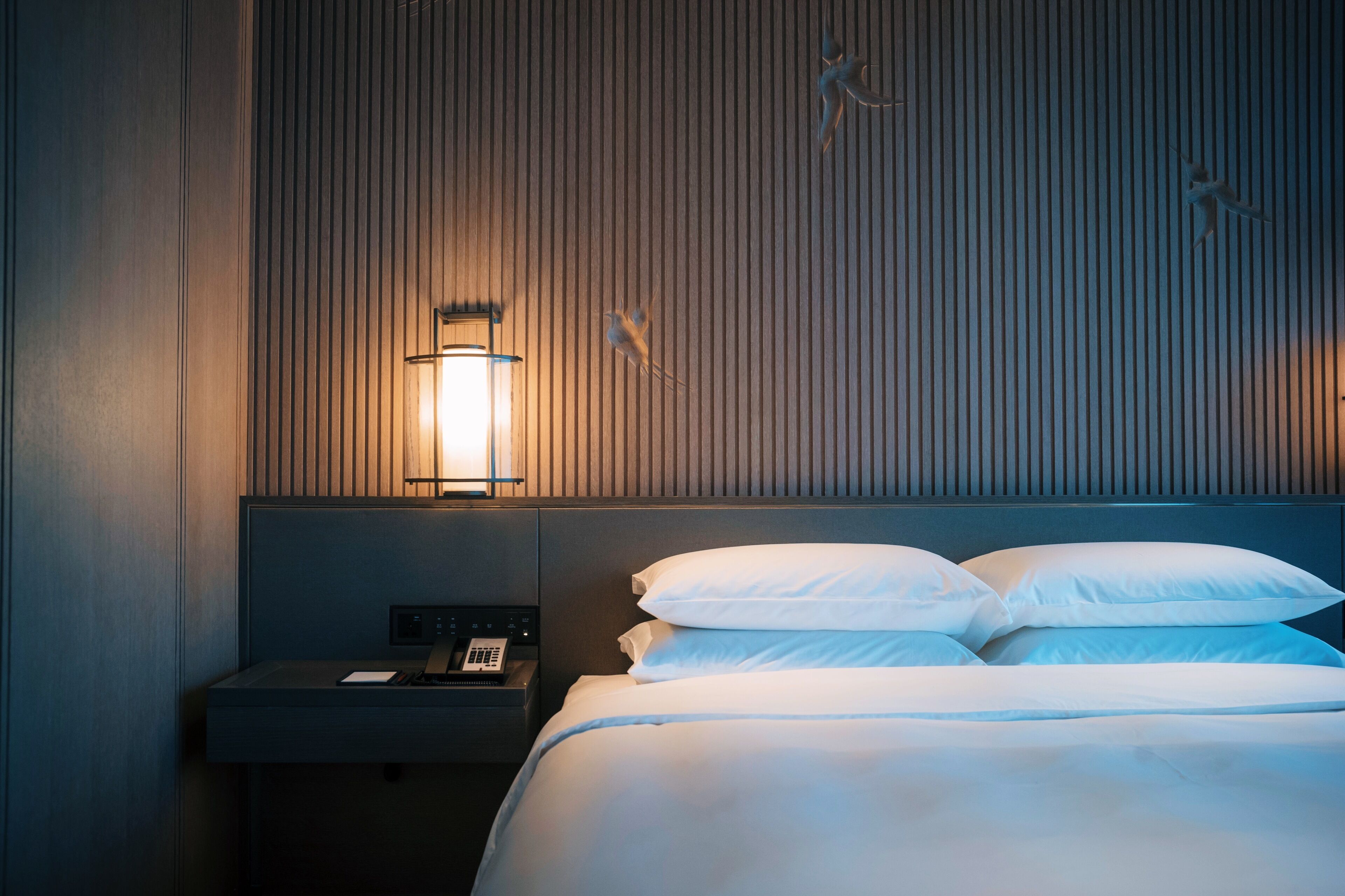 Una habitación de hotel con una cama, una mesita de noche con teléfono y una lámpara fijada a la pared.