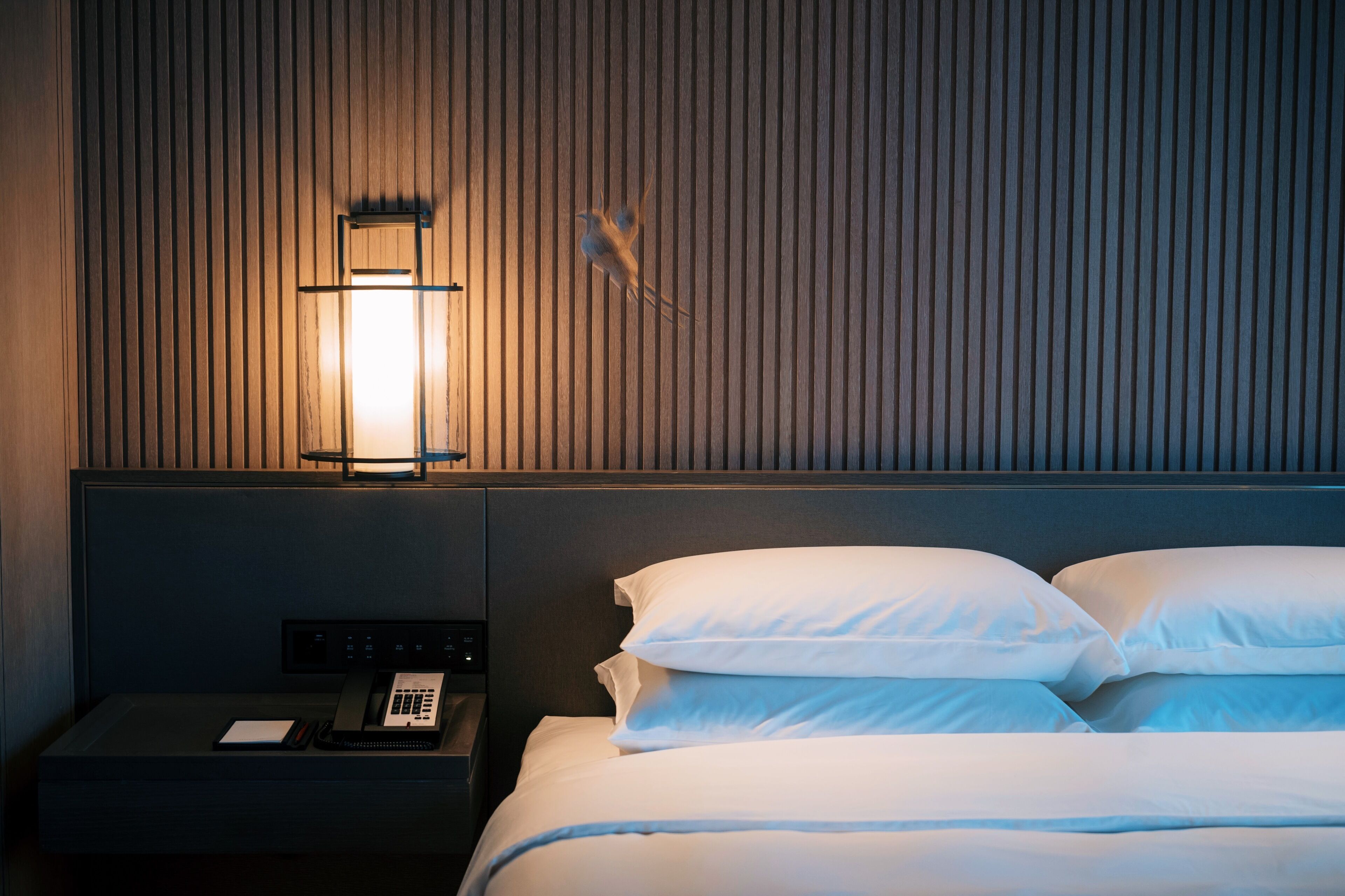 Habitación de hotel con una cama, una mesita de noche con teléfono y una lámpara de pared.