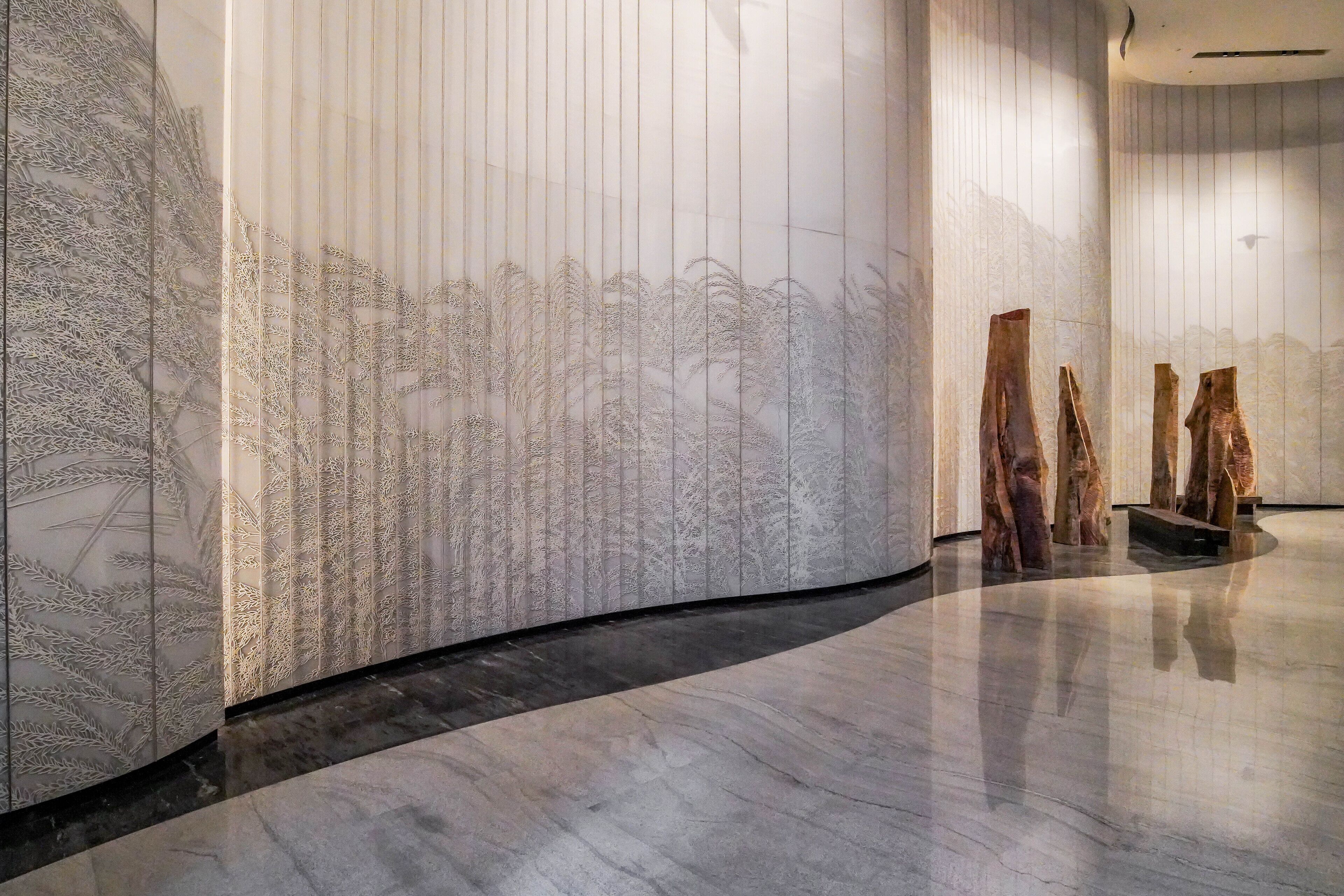 A modern interior with a curved wall featuring a detailed mural, a polished marble floor, and a few wooden sculptures.