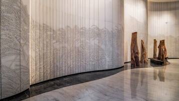 A modern interior with a curved wall featuring a detailed mural, a polished marble floor, and a few wooden sculptures.