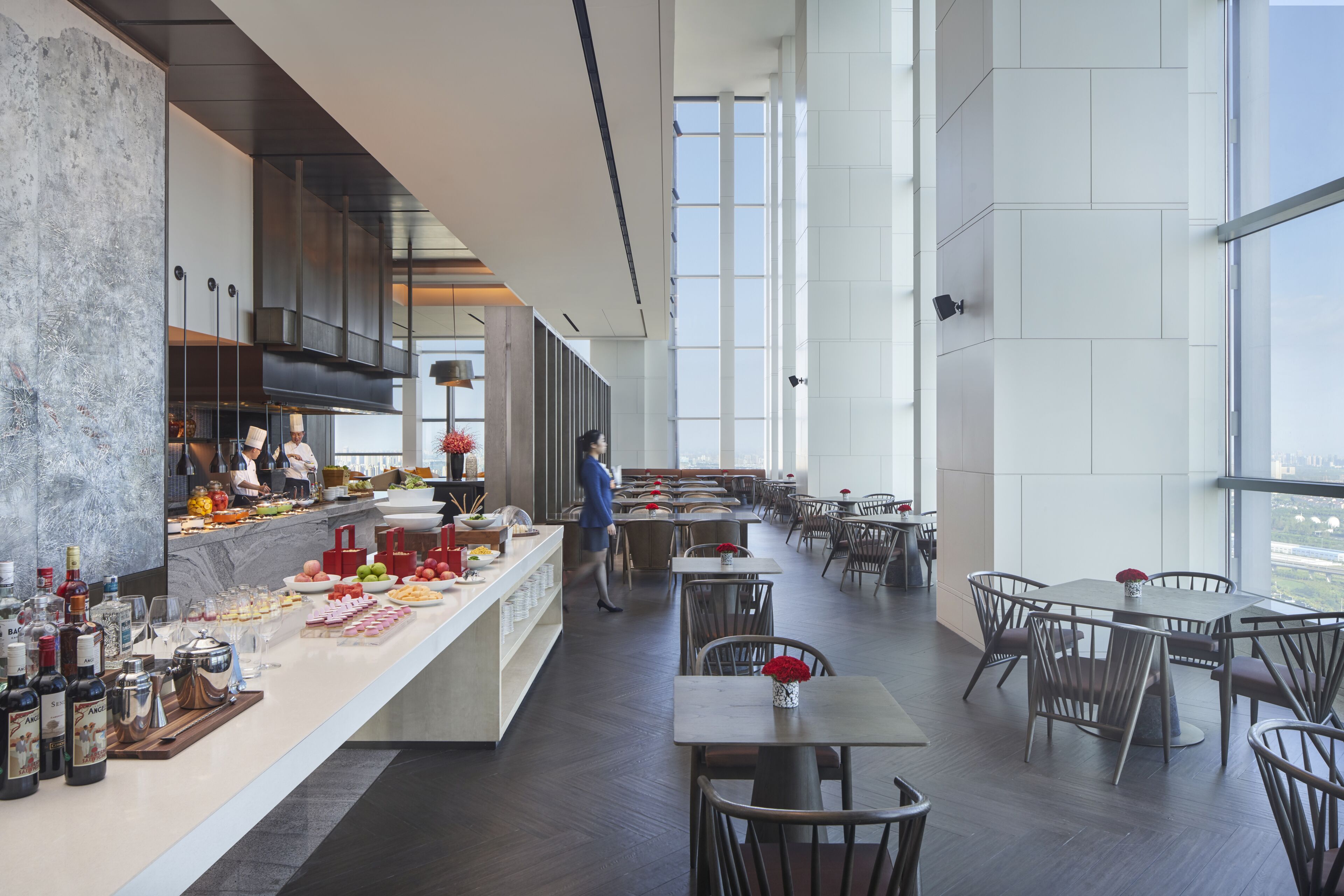 A modern restaurant with a long counter, dining tables, and chairs.