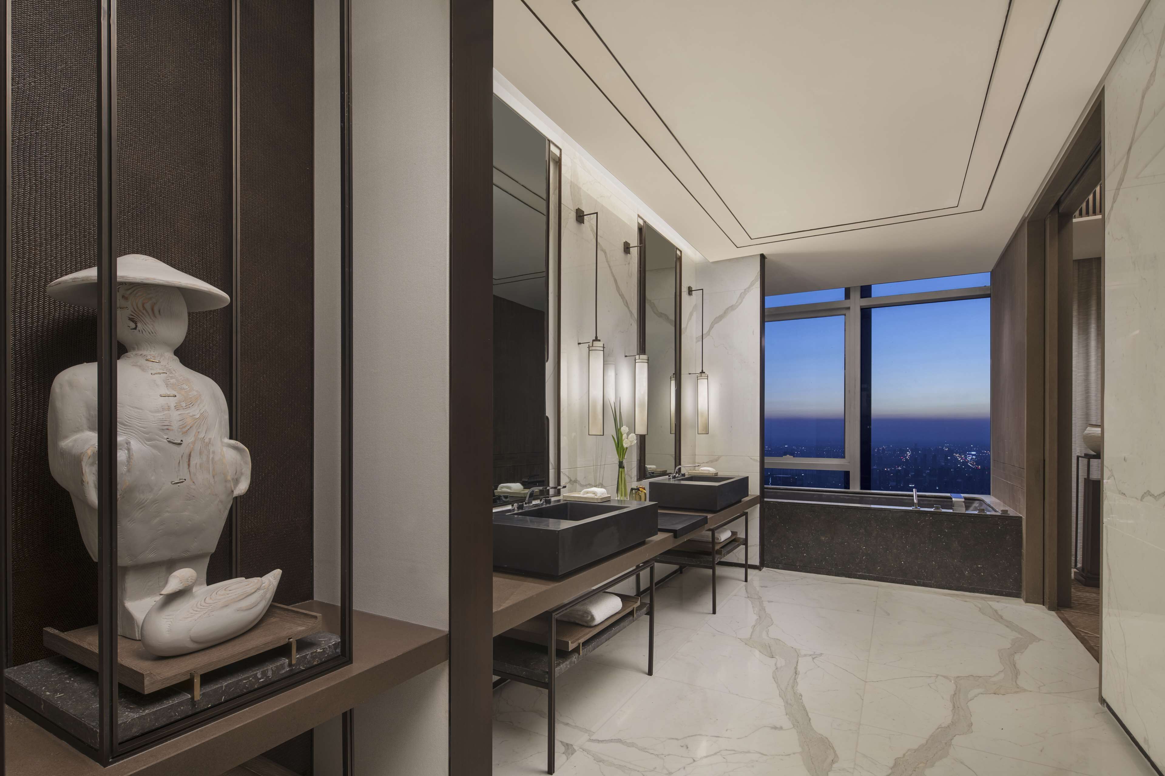 Ein modernes Badezimmer mit zwei Waschbecken, einem großen Spiegel und Blick auf die nächtliche Stadt.