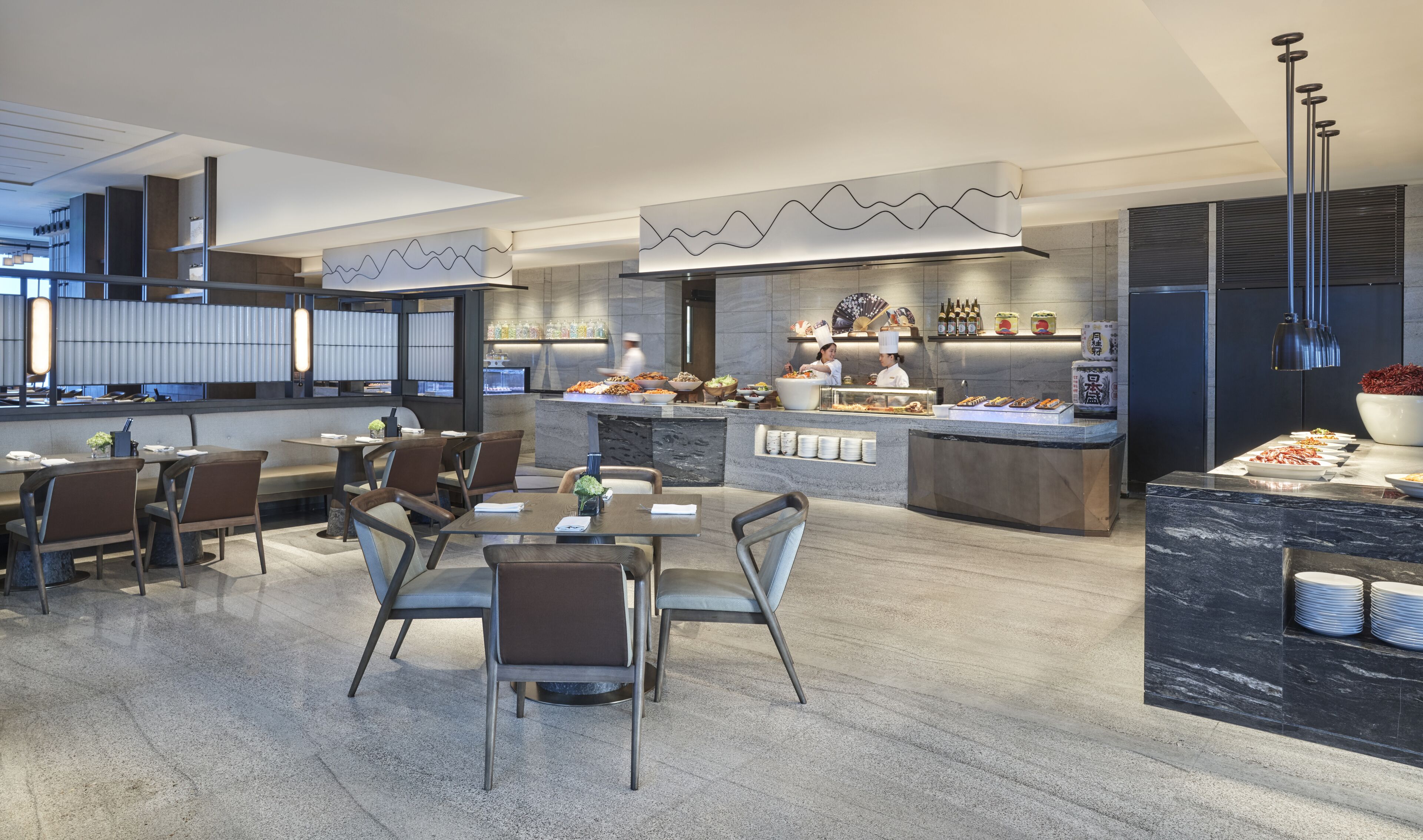 Un restaurante moderno con una zona de comedor central, una cocina al fondo y una barra con un bol grande de fruta.