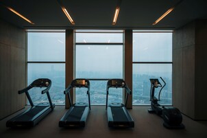 Un gimnasio con cintas de correr y una máquina elíptica, amplias ventanas con vista a la ciudad.
